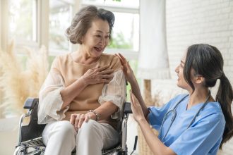 asian young caregiver caring for her elderly patient at senior daycare Handicap patient in a wheelchair at the hospital talking to a friendly nurse and looking cheerful nurse wheeling Senior patient